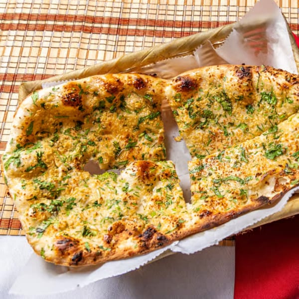Grilled flatbread topped with herbs and spices, cut into pieces and served on parchment over a checkered tablecloth.