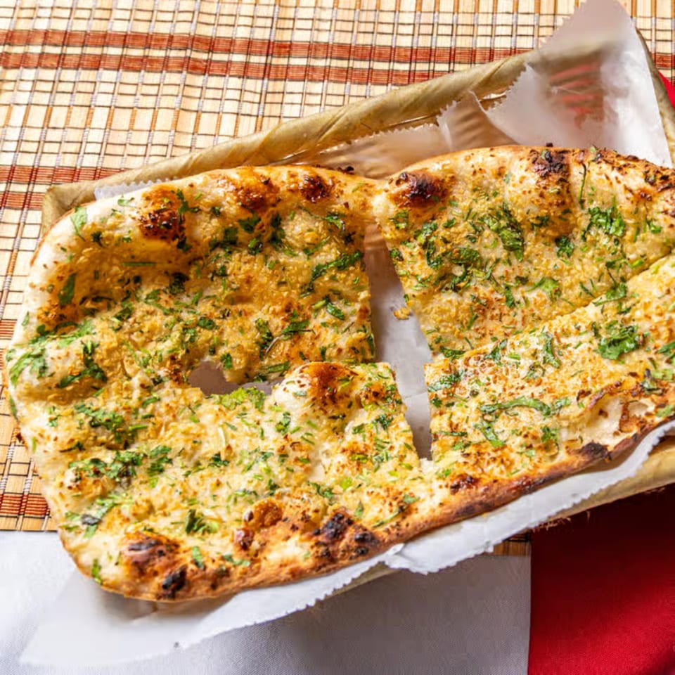 Grilled flatbread topped with herbs and spices, cut into pieces and served on parchment over a checkered tablecloth.