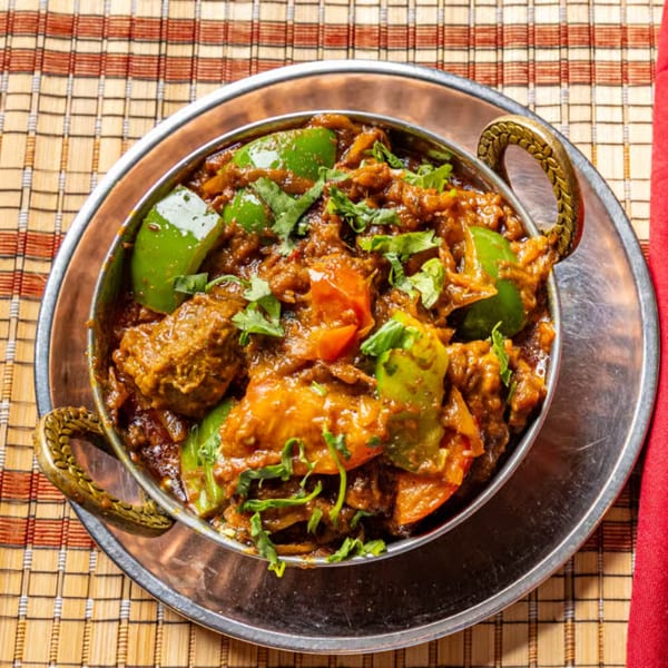 Close-up of richly spiced Indian curry with bell peppers and cilantro, served in a metal bowl on a woven placemat.
