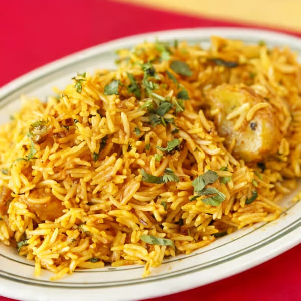Close-up of golden spiced rice garnished with fresh herbs and pieces of meat on a serving platter.
