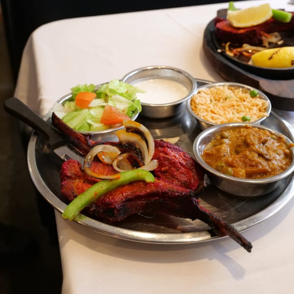 Indian thali platter with grilled tandoori meats, rice, curry, salad, creamy sauce, onions, and peppers on a metal tray.