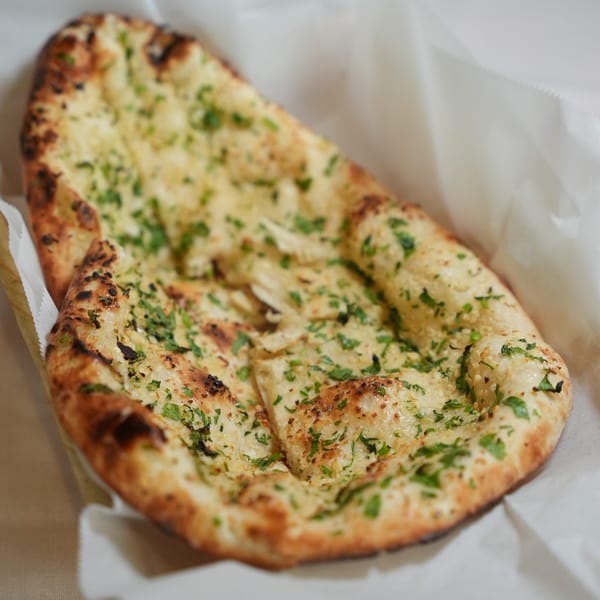Garlic naan breads topped with chopped herbs, served in a white paper-lined basket.