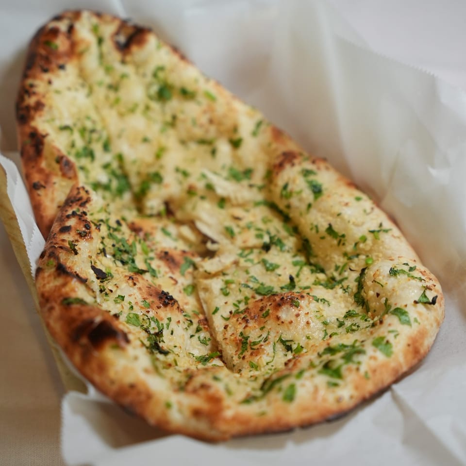 Garlic naan breads topped with chopped herbs, served in a white paper-lined basket.