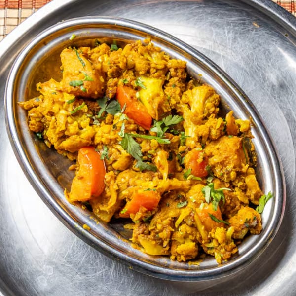 Golden spiced cauliflower and chicken curry with tomatoes and fresh cilantro, served in an oval metal dish.