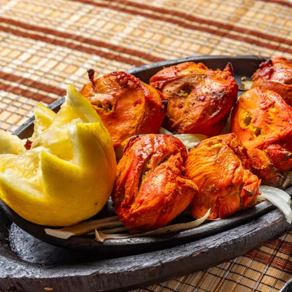 Tandoori-style grilled chicken pieces with lemon wedges served on a black platter atop a woven table mat.
