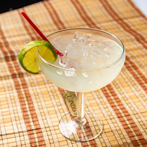 A refreshing margarita with a lime wedge and red straw, served on a woven placemat.