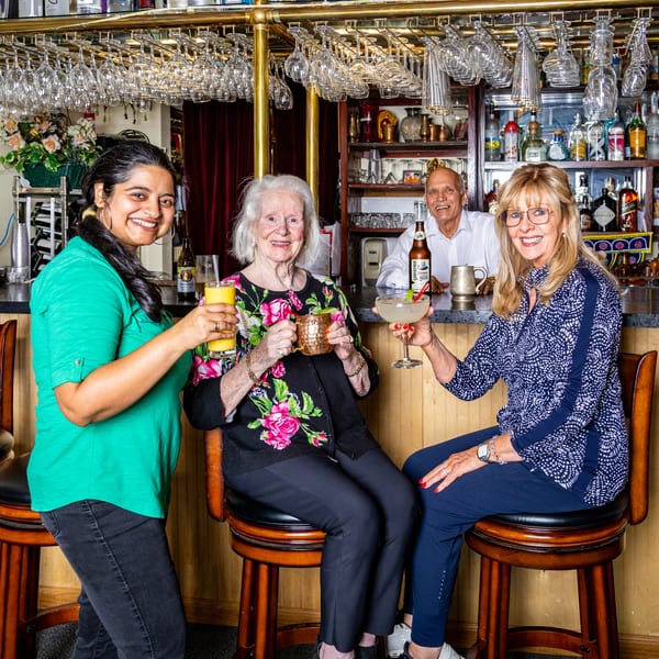 Three women and a man smiling with drinks at the INDIA'S Restaurant bar.