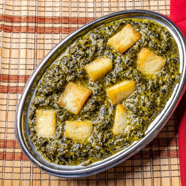 Palak Paneer, a vibrant green Indian spinach and cheese dish, in a silver oval bowl.