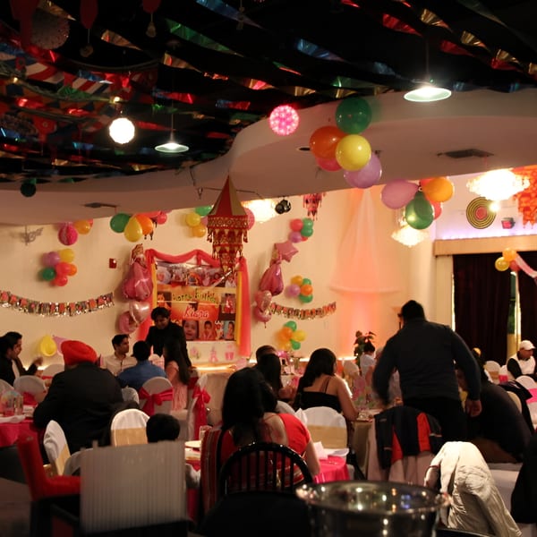 Guests seated at tables in a festive, balloon-decorated INDIA'S Restaurant dining room.