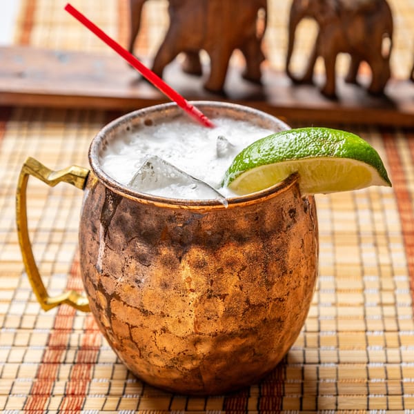 A copper mug filled with a white, frothy drink, ice, a red straw, and a lime wedge.