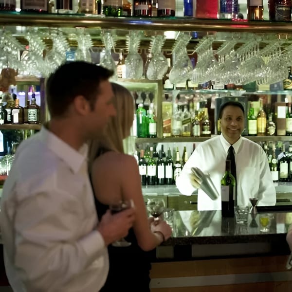 Bartender smiling behind a bar with a couple enjoying drinks at INDIA'S Restaurant.